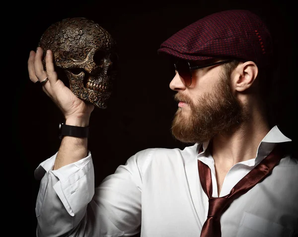 Жестокий мужчина с бородой и усами в шляпе и белой рубашке с галстуком на темном черепе — стоковое фото