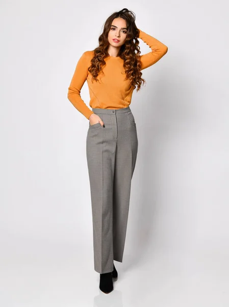 Jeune belle femme brune posant dans un nouveau pull chemisier orange décontracté et pantalon gris — Photo