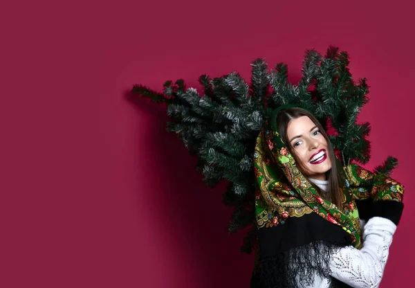 Gelukkig Russische stijl vrouw met sjaal greep kerstboom op haar schouders gelukkig lachen — Stockfoto