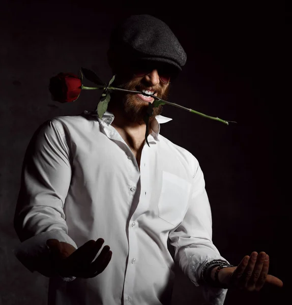 Uomo brutale con barba e cappello in possesso di rosa rossa in bocca per data — Foto Stock