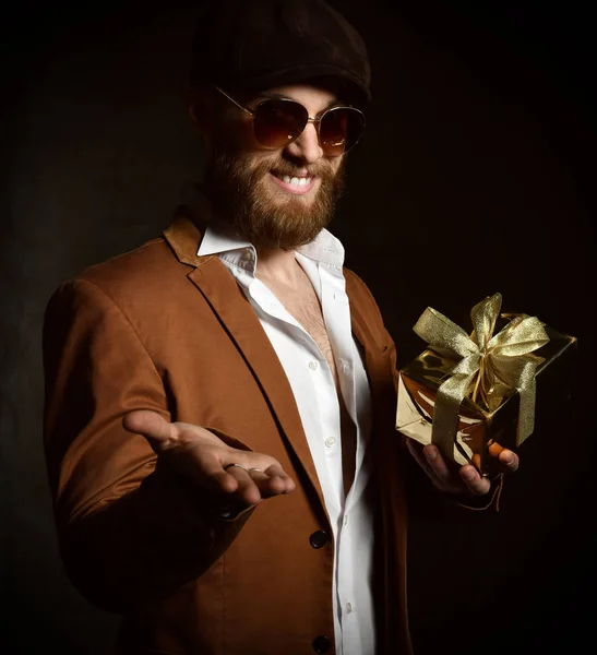 Жестокий человек с бородой и усами с золотым подарком на день рождения или Рождество открытая ладонь улыбаясь — стоковое фото