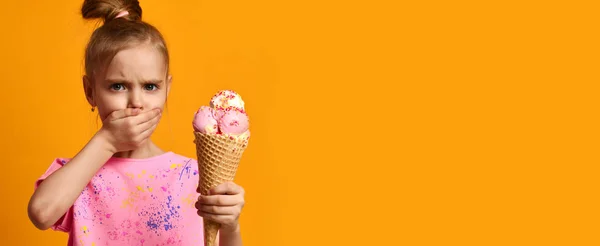 Симпатичная малышка держит клубничное мороженое в вафельном конусе на желтом фоне баннера — стоковое фото