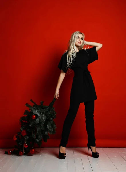Blonde vrouw in zwarte doek houd xmas Christmas tree op haar schouders — Stockfoto