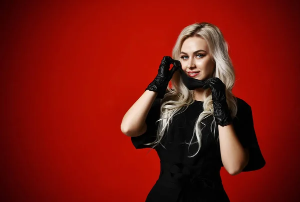 Hermosa mujer en máscara médica negra protectora y guantes sobre fondo rojo oscuro —  Fotos de Stock