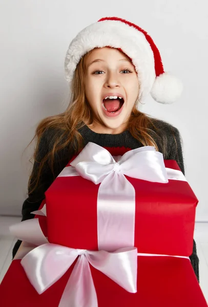 Lächelndes kleines Mädchen mit Weihnachtsmann-Helfermütze mit roten Geschenkboxen glücklich lächelnd schreiend schreiend — Stockfoto