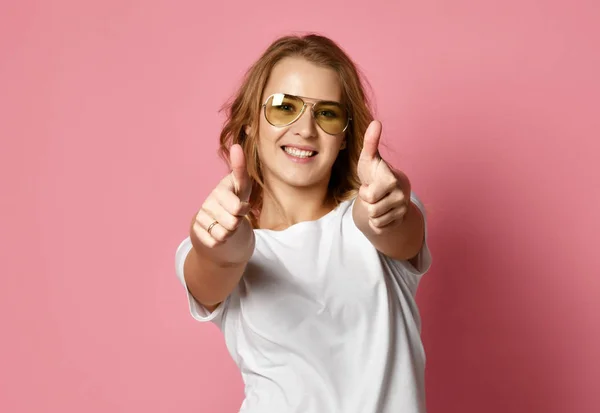 Mulher bonita em t-shirt branca e óculos de sol aviador mostrar polegares para cima sinal em rosa — Fotografia de Stock