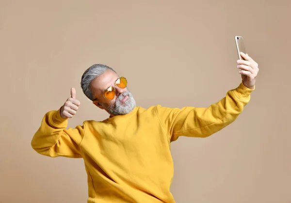 Porträtt av happy senior miljonär man använder smartphone mobiltelefon gör selfie i gula solglasögon — Stockfoto