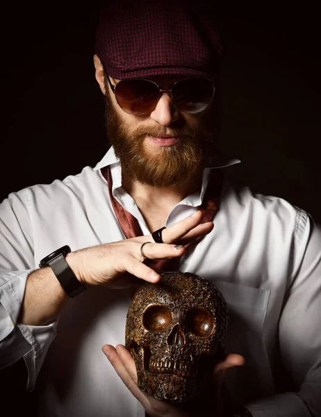 Hombre brutal con barba y bigote en gorra de sombrero y camisa blanca con corbata en calavera oscura —  Fotos de Stock