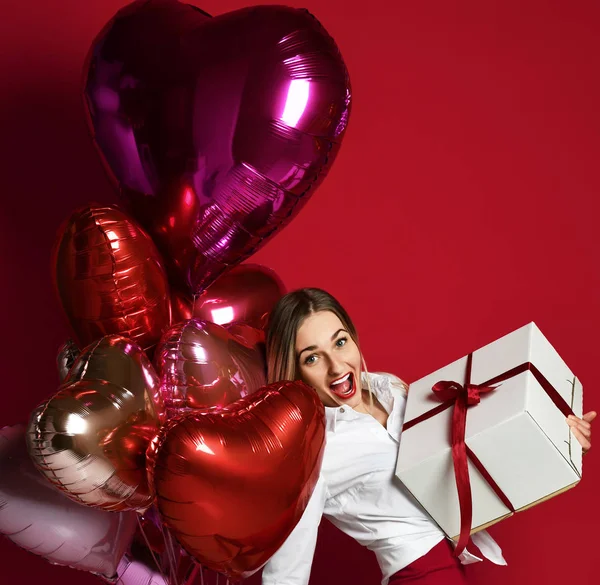 Bella donna con regalo regalo scatola e viola rosa palloncini cuore felice sorridente su sfondo rosso — Foto Stock