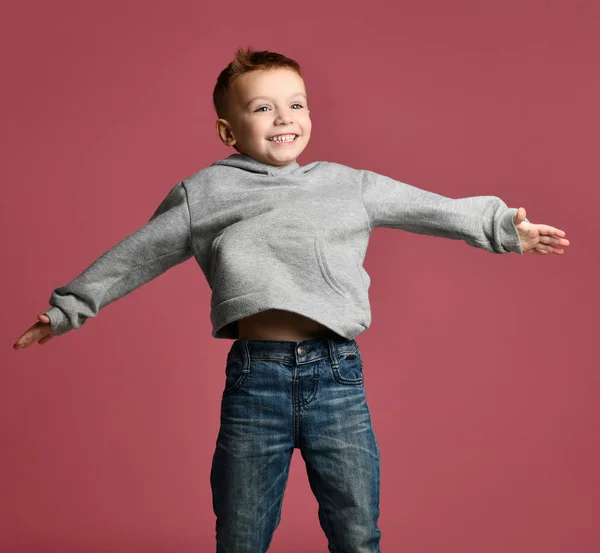 Młody chłopak dziecko skoki w szara Bluza z kapturem z rąk rozprzestrzeniania się śmiejąc się uśmiecha się na NK — Zdjęcie stockowe