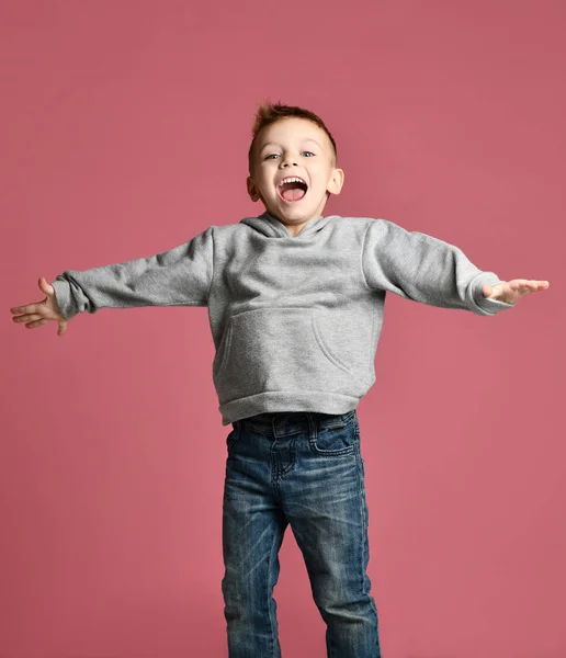 Jovem garoto pulando em capuz cinza com as mãos espalhadas rindo-se sorrindo no rosa — Fotografia de Stock