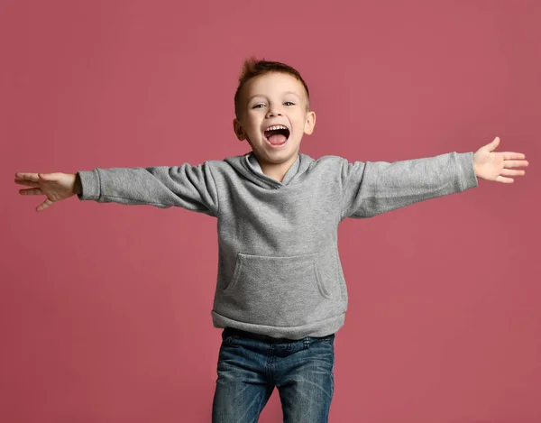 Niño saltando en sudadera gris con las manos extendidas riendo sonriendo en rosa — Foto de Stock