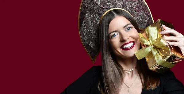 Mooie vrouw houd goud aanwezig geschenkdoos in Russische traditionele zwarte kokoshnik hoed gelukkig lachend — Stockfoto