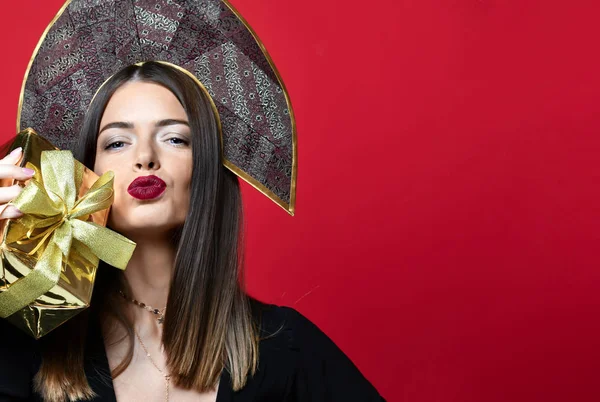Mooie vrouw houd goud aanwezig geschenkdoos in Russische traditionele zwarte kokoshnik hoed gelukkig kussen — Stockfoto