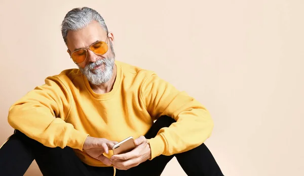 Retrato de homem milionário sênior feliz usando celular smartphone digitando mensagens de texto em óculos de sol amarelos — Fotografia de Stock