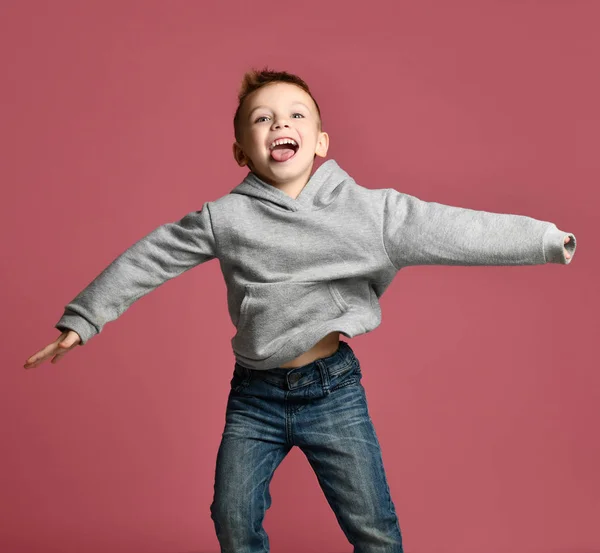 Mladý chlapec dítě skákání v šedá mikina s rukama šíří se směje, usmívající se na růžový — Stock fotografie