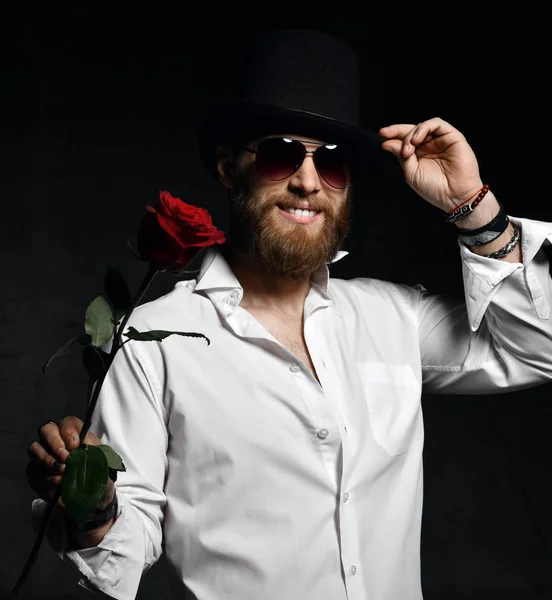 Brutal hombre con barba y sombrero sosteniendo rosa roja para la fecha —  Fotos de Stock