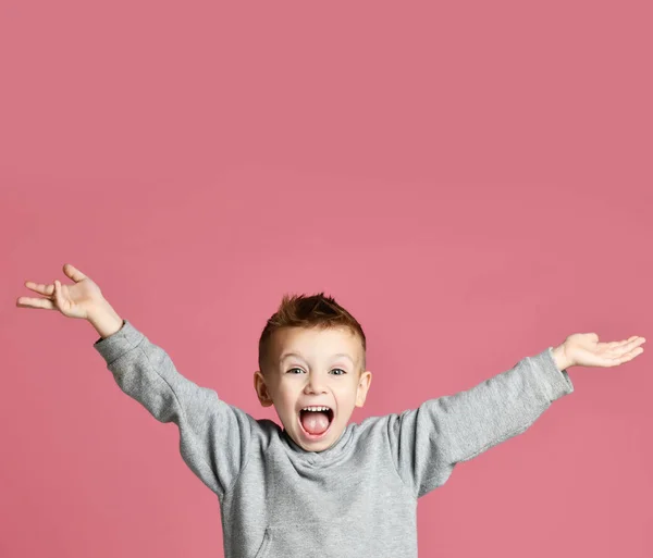 Niño saltando en sudadera gris con las manos extendidas riendo sonriendo en rosa — Foto de Stock