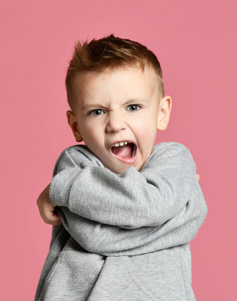 Baby boy kid warlike angry shouting  screaming in gray hoodie over pink 