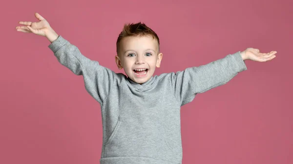 Jongen jongen springen in grijs hoodie met handen verspreiden van lachen glimlachend op roze — Stockfoto