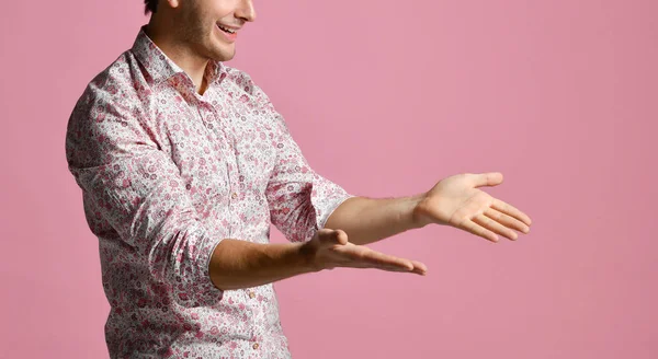 Hombre joven con camisa tienen un diálogo gesticulando con las manos abiertas palmas sonriendo en rosa —  Fotos de Stock