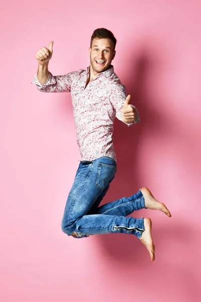 Feliz hombre ganador celebrando un acuerdo exitoso ganando señalando las manos con los dedos hacia arriba sobre rosa — Foto de Stock