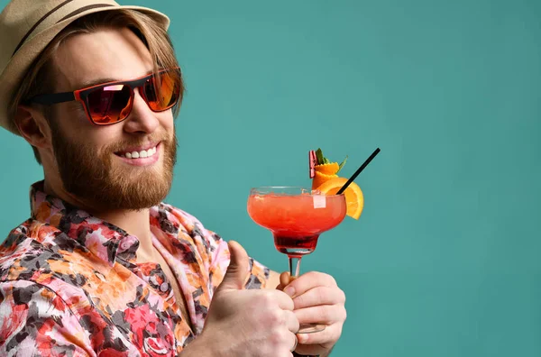 Young man in hat show thumb up drinking red margarita cocktail drink juice happy looking at camera over blue — Stock Photo, Image