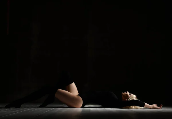 Молодая сексапильная блондинка, лежащая на полу в черной одежде и шапке. — стоковое фото