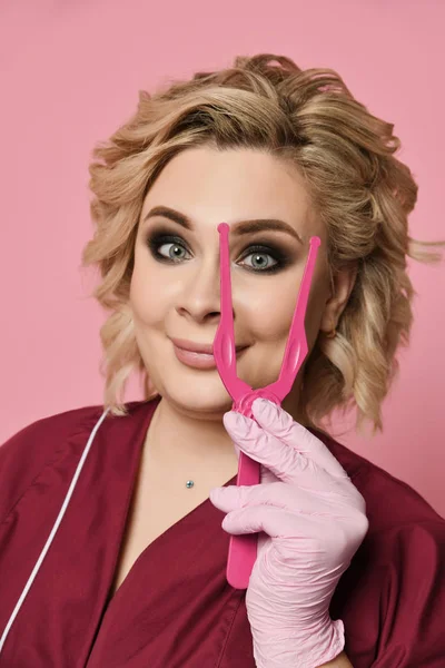 Жінка-косметолог тримає велику рожеву косметологію пінцет щасливий — стокове фото