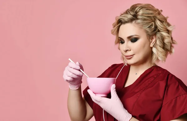 Жінка-косметолог тримає велику рожеву косметологічну миску, змішуючи крем для обличчя — стокове фото