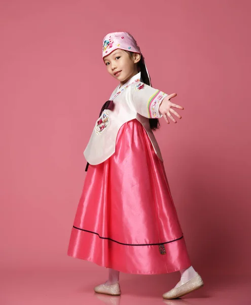 Bambina coreana in abito tradizionale di seta per festeggiare il nuovo anno danzando sul rosa con le mani distese — Foto Stock