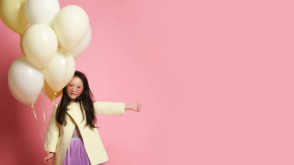 Küçük Asya bebek kız sarı moda ceket ve mor elbise balonlar ile kutlamak mutlu gülümseyen başparmak yukarı — Stok fotoğraf