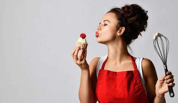 Koki wanita muda memegang kue cangkir manis dengan krim dan kawat kocok telur pemukul terkejut — Stok Foto