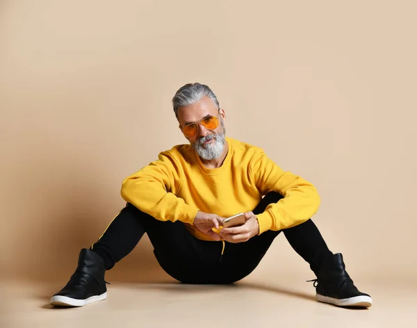 Portrait of happy senior millionaire man using smartphone cellphone typing texting in yellow sunglasses — Stock Photo, Image