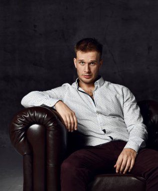 Deri Chester koltuk kanepe koyu arka plan üzerinde rahat gömlek düşüncesinde oturan genç iş adamı