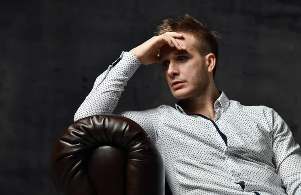 Young business man sitting in leather Chester armchair sofa in casual shirt thinking — Stock Photo, Image