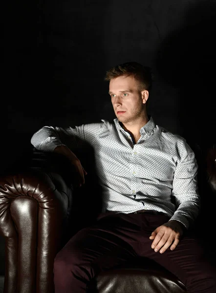 Young business man sitting in leather Chester armchair sofa in casual shirt thinking — Stock Photo, Image