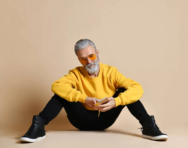 Retrato de homem milionário sênior feliz usando celular smartphone digitando mensagens de texto em óculos de sol amarelos — Fotografia de Stock