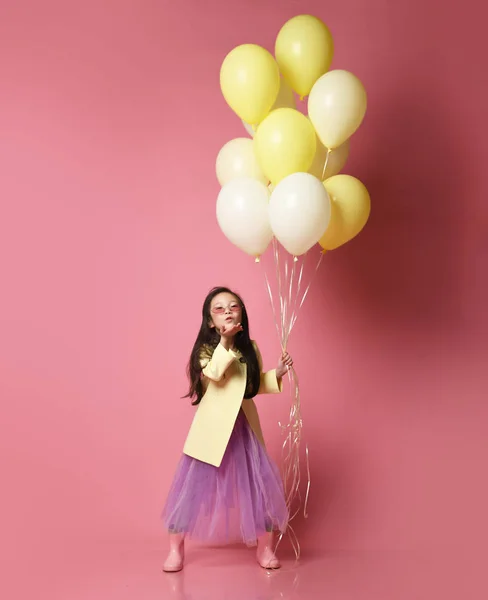 Petite fille asiatique en veste de mode jaune et robe violette avec ballons célébrer heureux sourire soufflant baiser — Photo