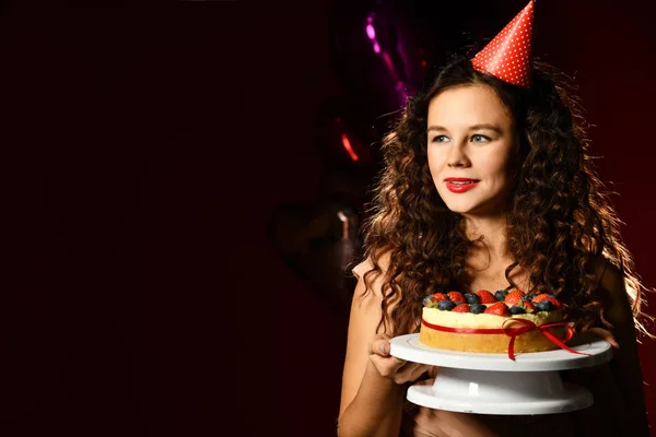 Young woman chef cook hold sweet cake with strawberry blueberry and cream celebrating smiling with balloons