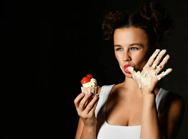 Genç kadın şef aşçı tutun tatlı kek krem çilek yalamak parmak ile siyah — Stok fotoğraf