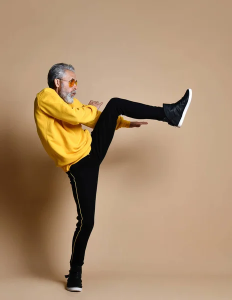 Üst düzey milyoner adam sarı bez ve havacı şık güneş gözlüğü germe egzersiz bacak yumrukla vurdu — Stok fotoğraf