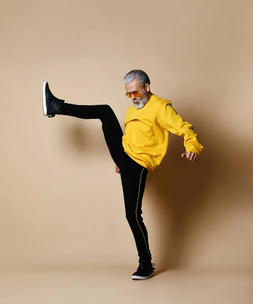 Senior millionaire man in yellow cloth and aviator stylish sunglasses exercise stretching hit punch with leg — Stock Photo, Image