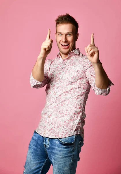 Joven feliz sonriente hombre en camisa afortunado ganador apuntando dedo pulgar hacia arriba riendo gritando en rosa — Foto de Stock