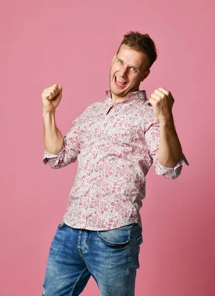 Joven feliz sonriente hombre en camisa afortunado ganador apuntando dedo pulgar hacia arriba riendo gritando en rosa — Foto de Stock