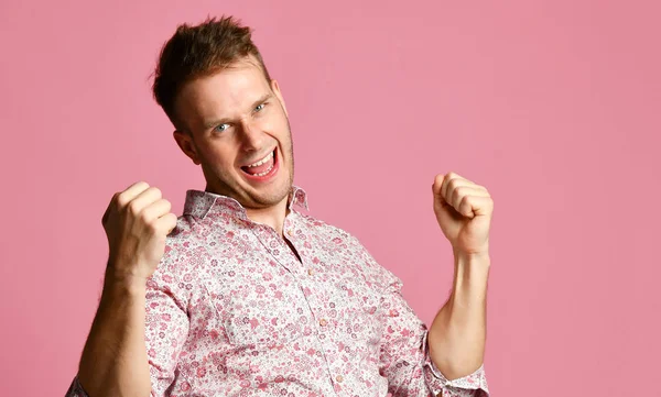 Joven feliz sonriente hombre en camisa afortunado ganador apuntando dedo pulgar hacia arriba riendo gritando en rosa — Foto de Stock