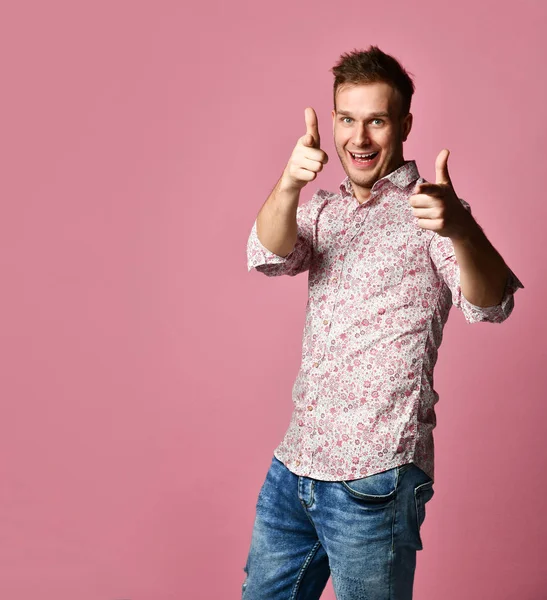 Joven feliz sonriente hombre en camisa afortunado ganador apuntando dedo pulgar hacia arriba riendo gritando en rosa — Foto de Stock