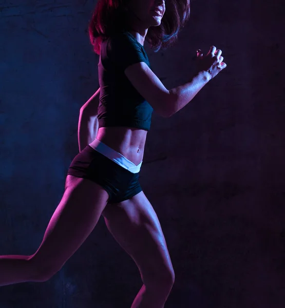 Молодая спортивная женщина бегает в гинекологе в голубом и розовом неоновом свете на темной стене — стоковое фото