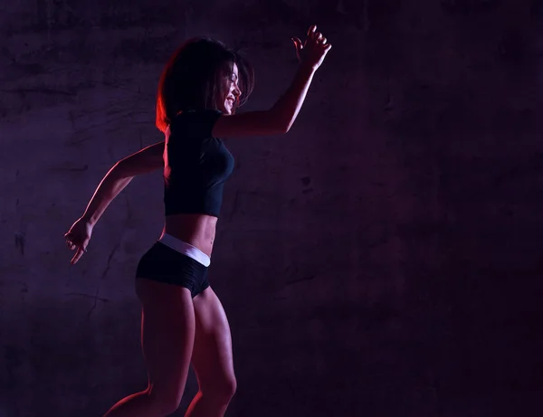 Jovem mulher esporte correndo correndo em ginástica em azul e rosa luz de néon na parede escura — Fotografia de Stock