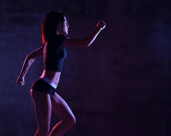 Jovem mulher esporte correndo correndo em ginástica em azul e rosa luz de néon na parede escura — Fotografia de Stock